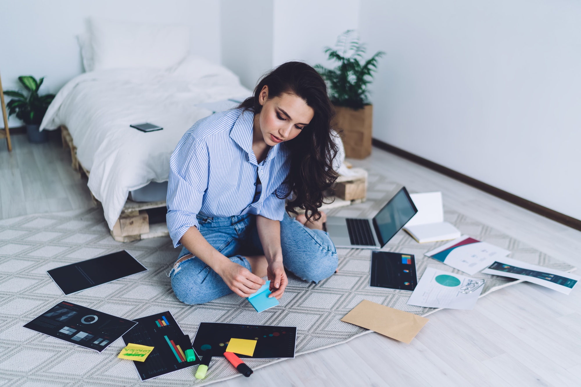 Concentrated student sticking stickers on drawing sitting on floor with laptop